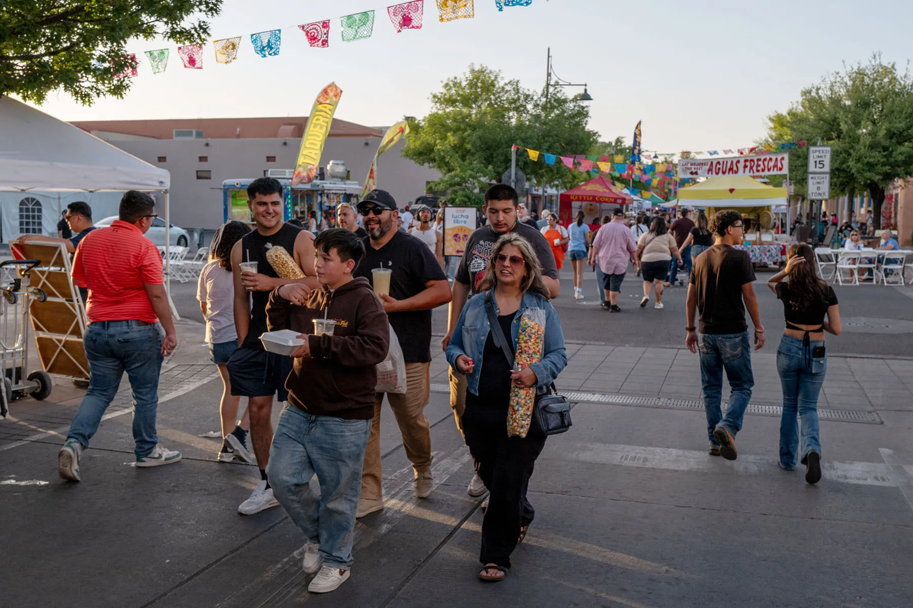 Several people walk through the streets during a street festival, carrying food and drinks.