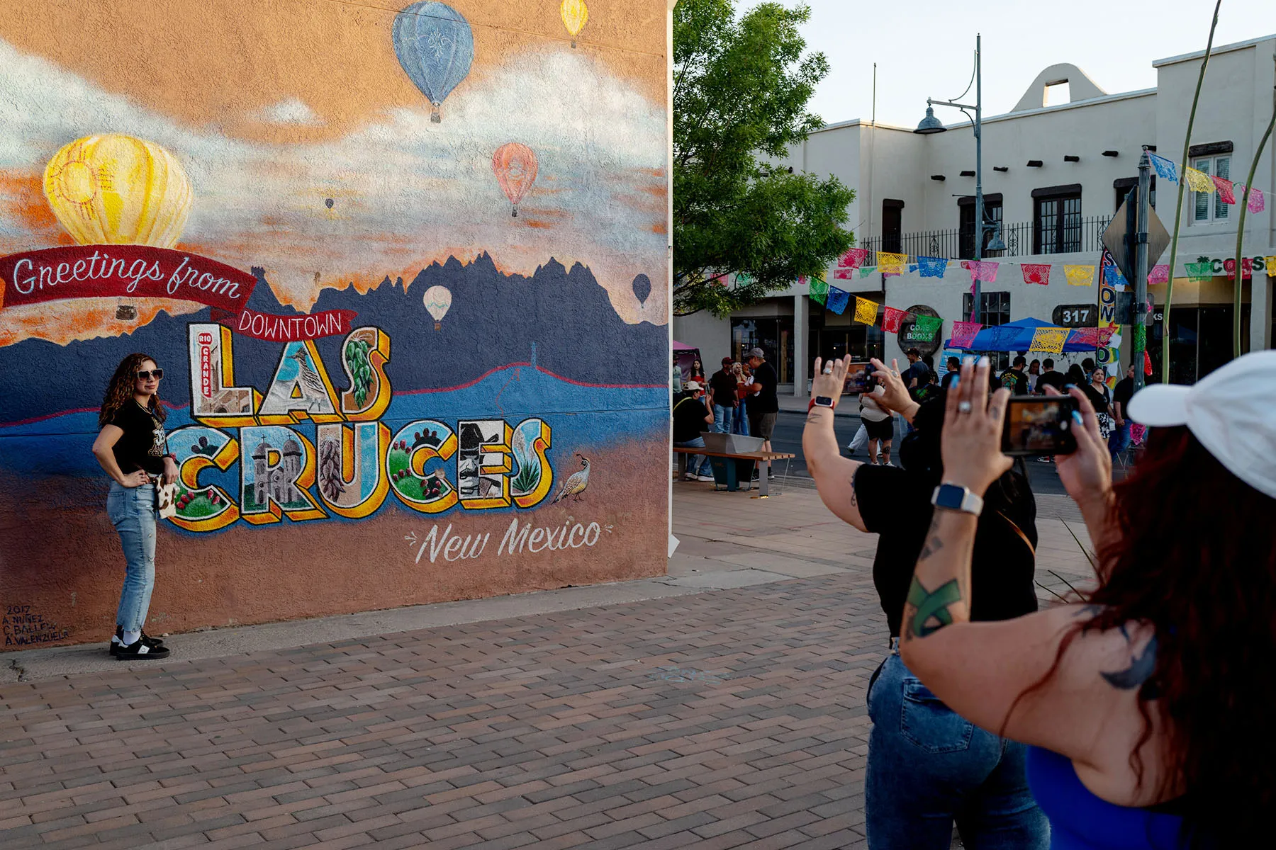 People take photos in front of a wall mural that says greetings from "Las Cruces."
