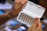A woman holds a one-month’s prescription of birth control pills.